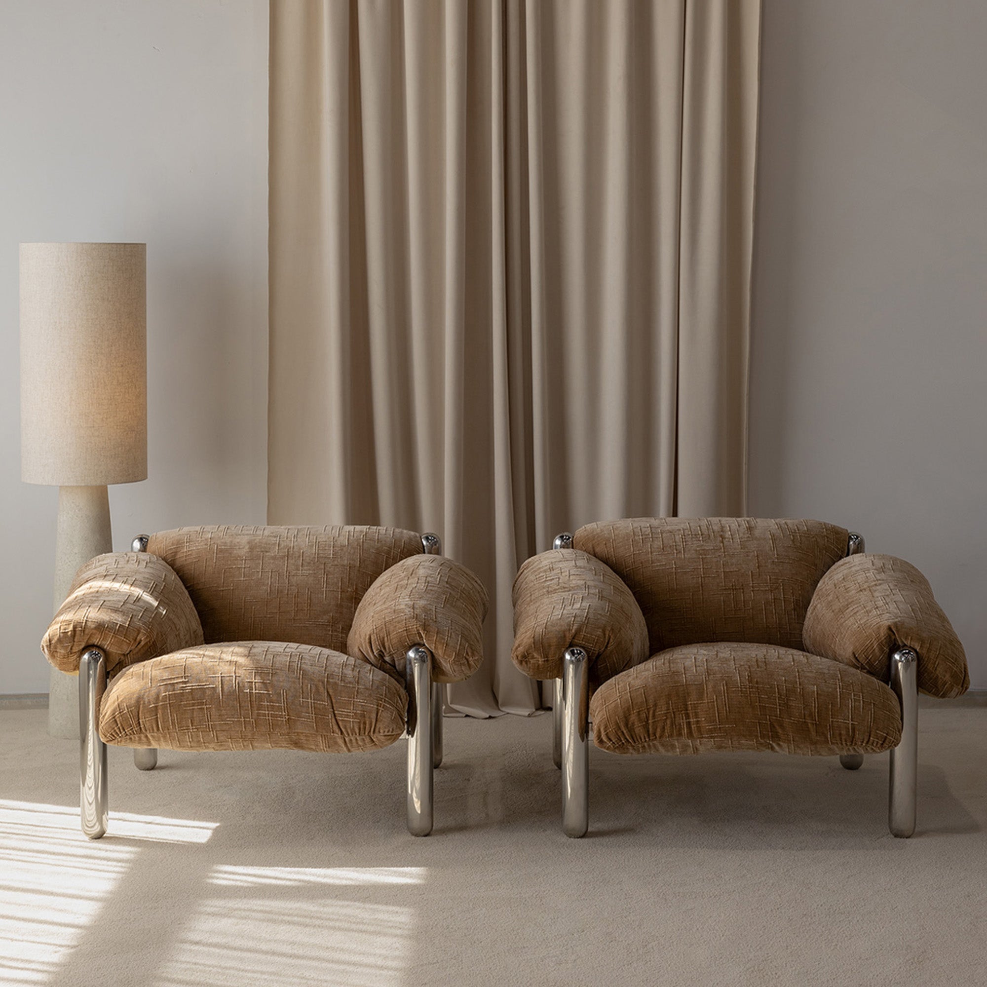 2 Raf Chairs side-by-side in a naturally lit room with a textured lamp and draped curtain in the background.